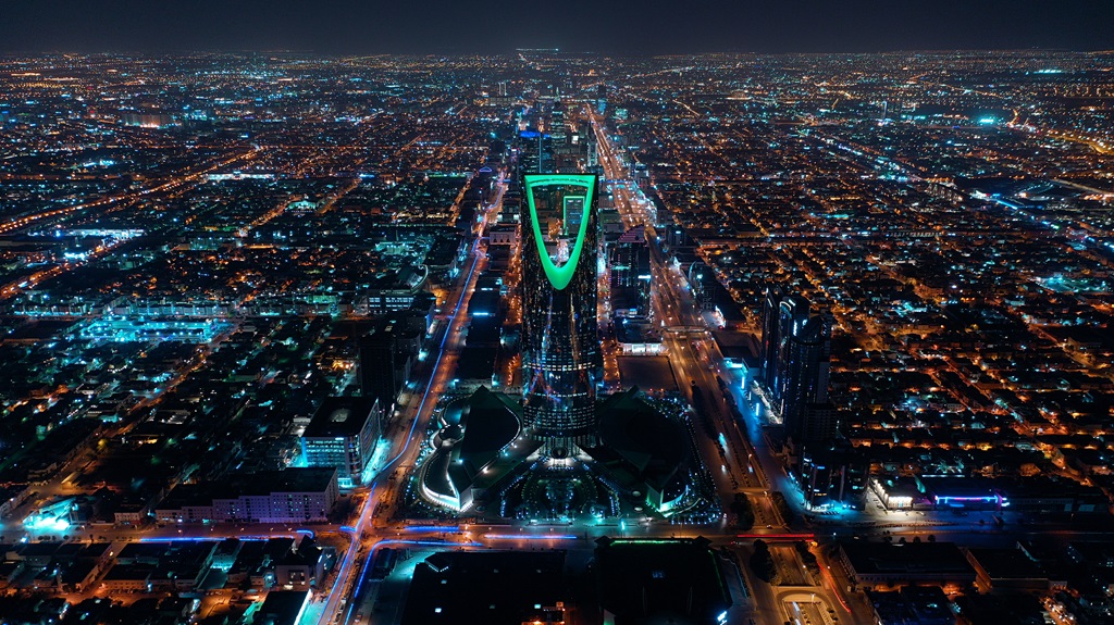 A dramatic aerial view of Riyadh at night, with the illuminated Kingdom Tower in the center